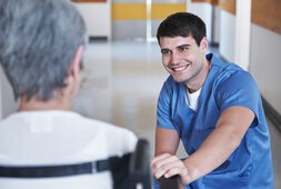 Azubi in Pflegeausbildung kniet lachend vor Patientin | © Shapecharge/Getty Images iStock 536458141